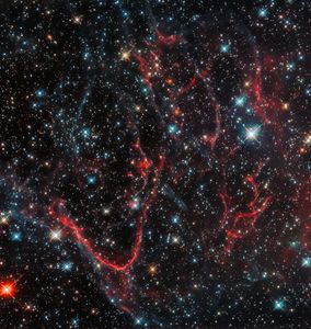 Red and blue streamers of gas and dust in space, with bright multicolored stars scattered throughout.